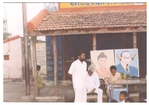 Datta Ahiwale speaking at a community event with portraits of social reformers